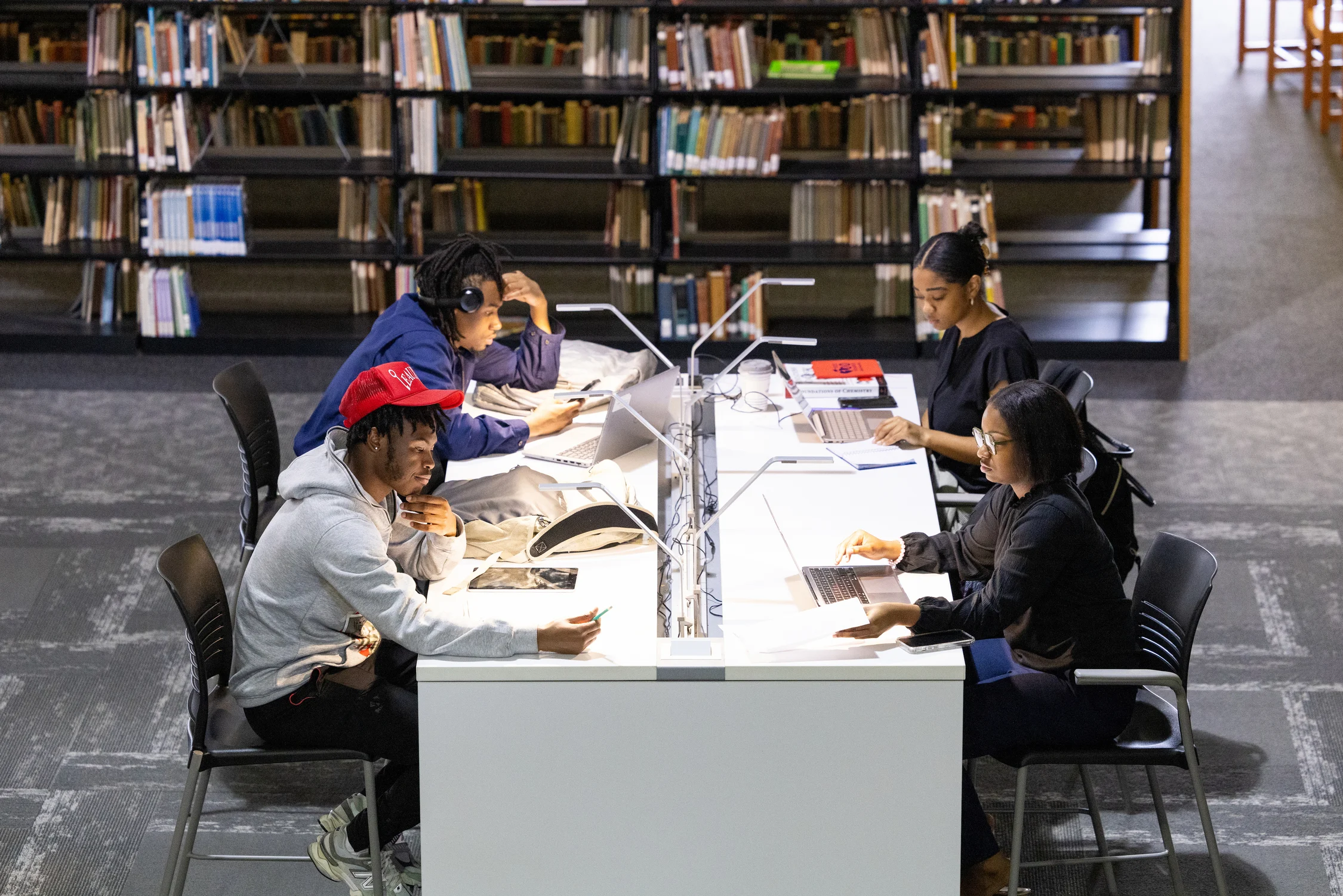 A college student studying at a quiet library table with a notebook, laptop, and a cup of coffee, concentrating on reading