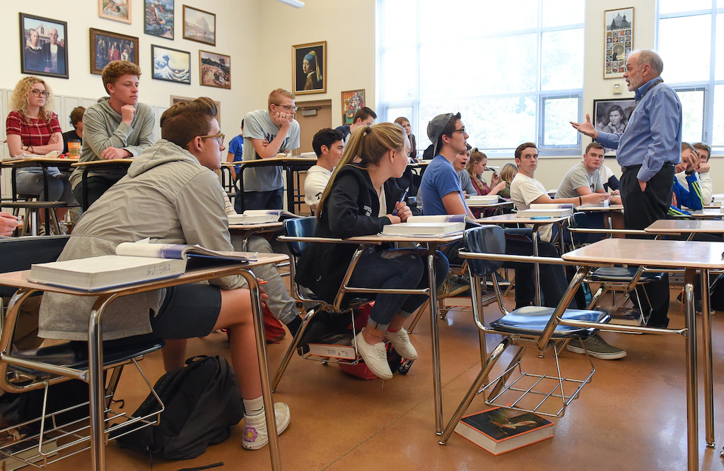 A high school student seated at a classroom desk during an AP exam session, focused on a test booklet and answer sheet in a quiet testing room