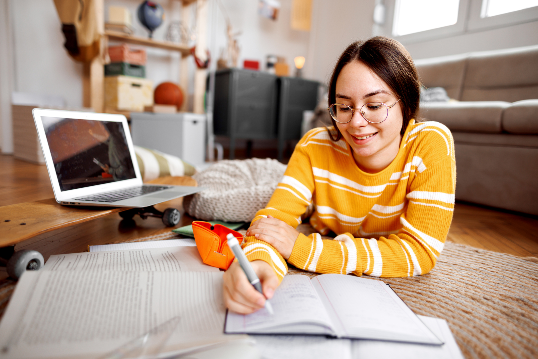 A high school student studying at a desk with a laptop and notebooks in a quiet home setting