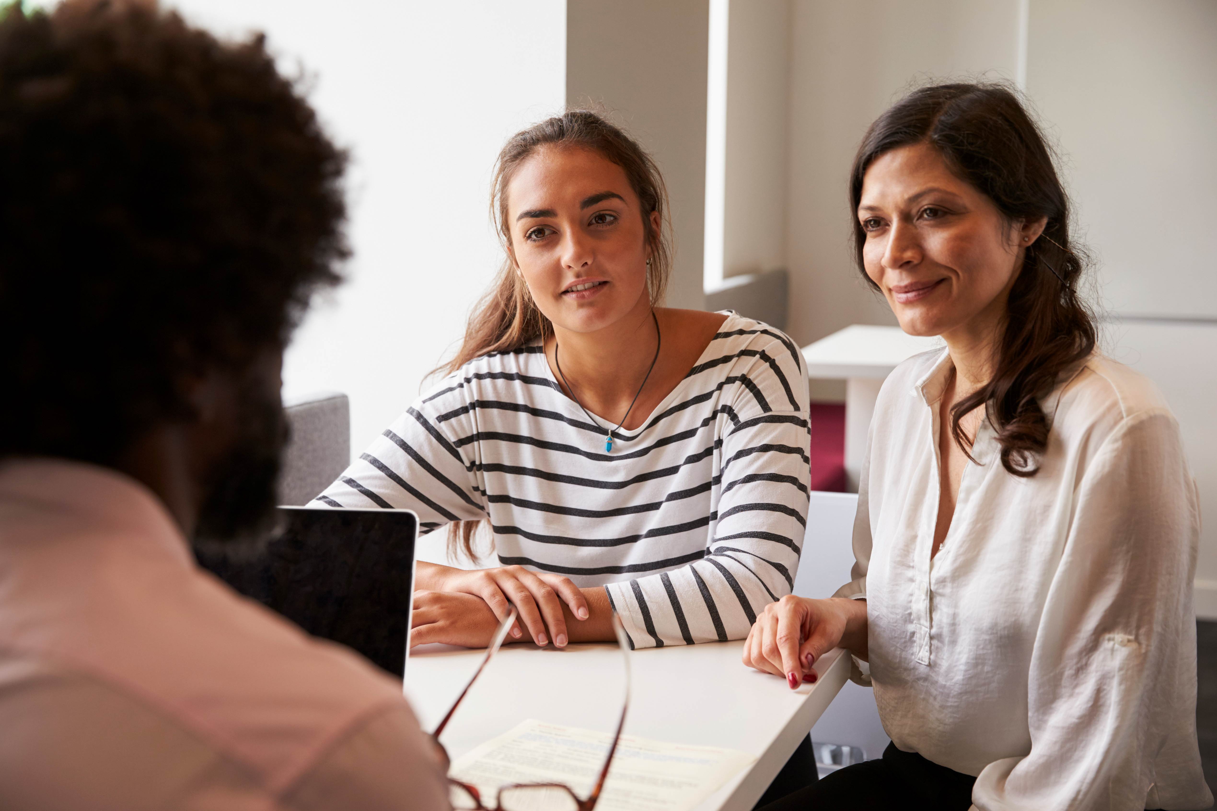 A parent and high school student sitting across from a school counselor in an office, reviewing course planning papers