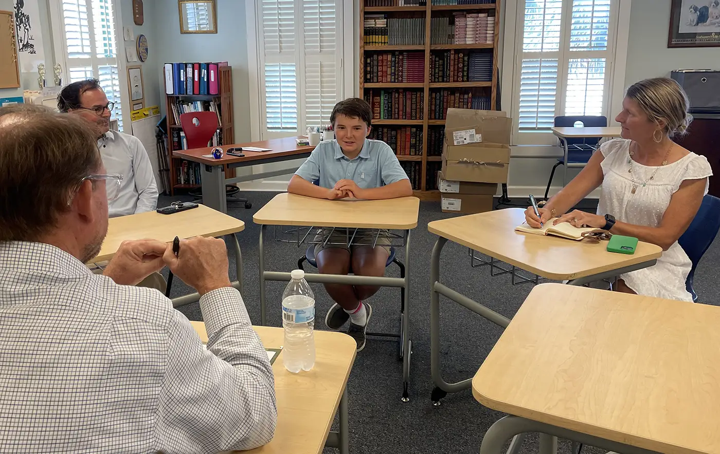 A parent and high school student sitting across from a school counselor in an office, reviewing course planning documents together