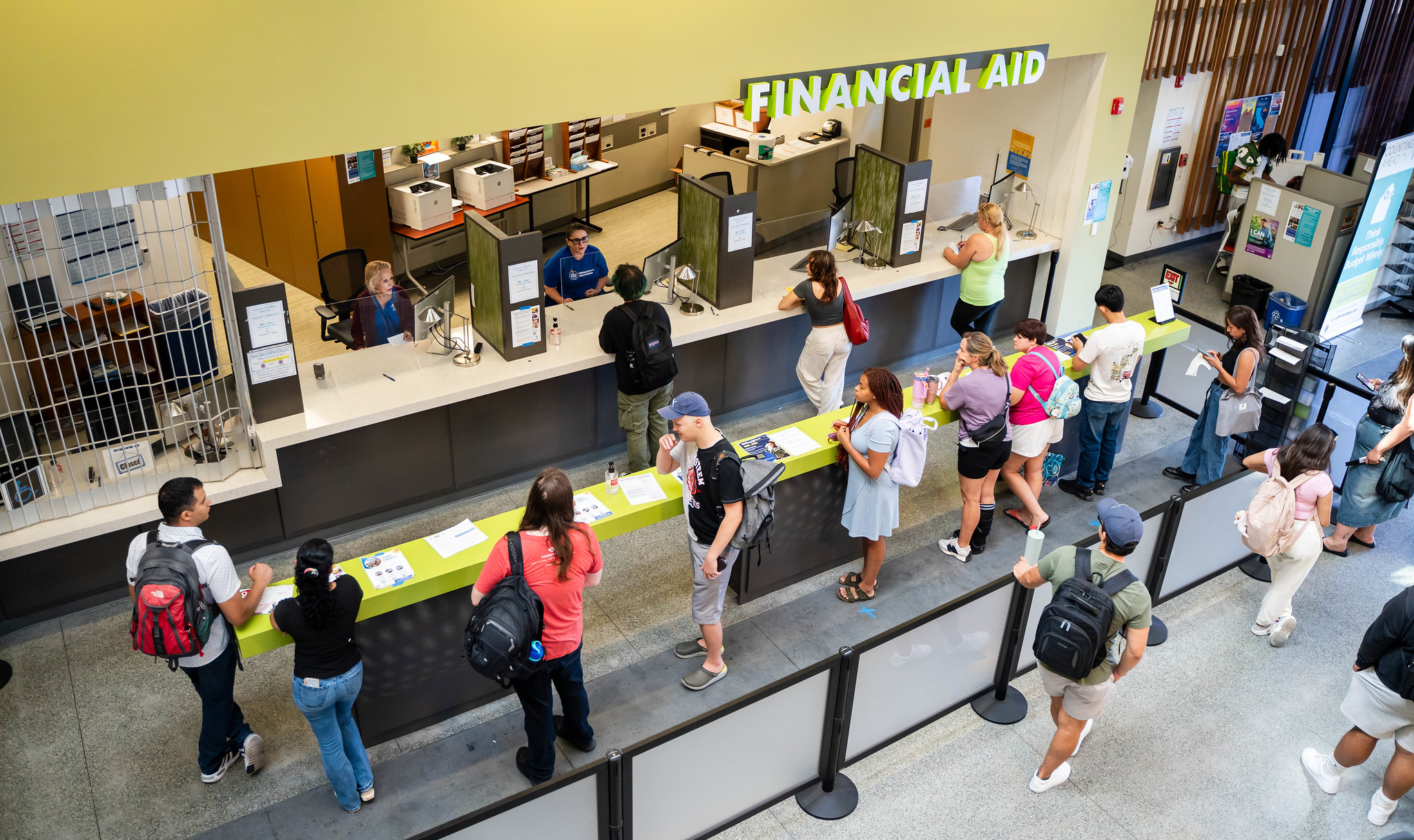 A student and a parent sit across from a financial aid counselor at a desk with paperwork and a laptop, discussing an award letter