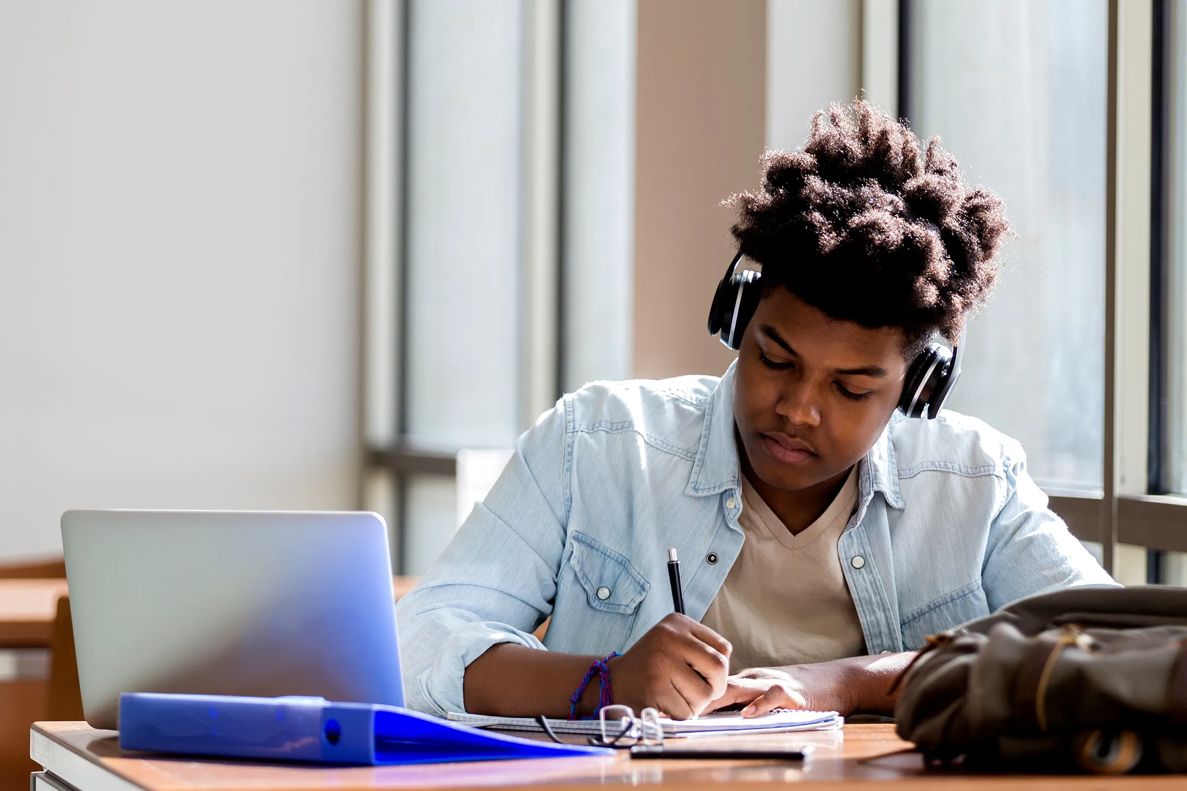 A student looking at a school assignment dashboard on a laptop while holding a pen over a notebook, planning what to do next