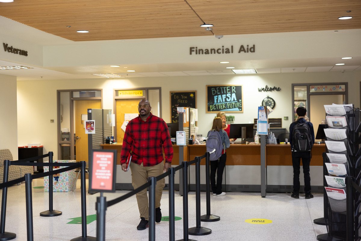 A student walking into a university financial aid office in a campus administration building hallway during daytime