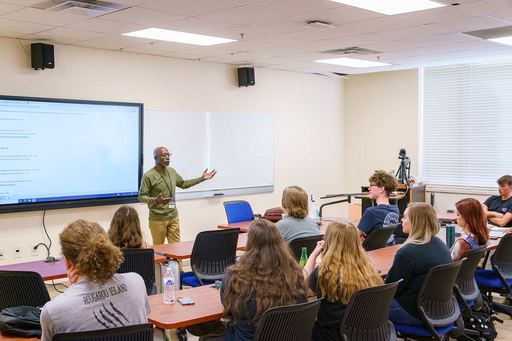 An instructor teaching in a community college classroom while students take notes